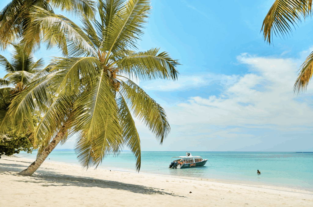 A quiet boat floats on the turquoise waters of Nosy Be — pure serenity under the island sun, with Discover Madagascar. Tropical beach with turquoise water, a small boat, and blue sky in Nosy Be, Madagascar — with Discover Madagascar